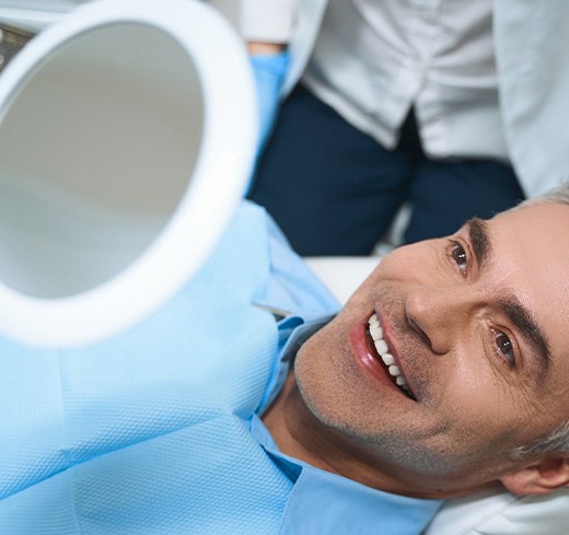 Man in dental chair smiling into handheld mirror