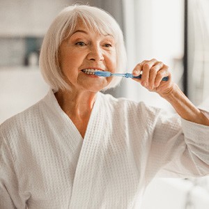 Older woman in a robe and brushing her teeth