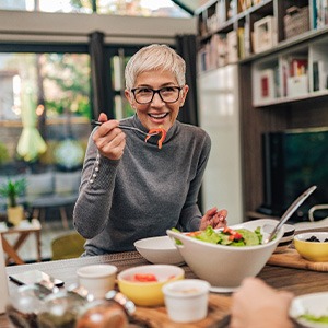 Woman with black glasses smiling while eating with friend