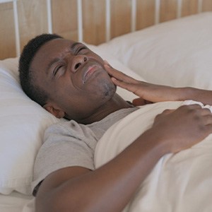 Man experiencing jaw pain in bed after grinding his teeth throughout the night