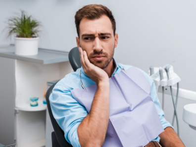 Man in dental chair rubbing jaw in pain