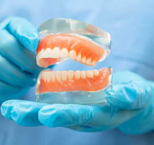 Gloved hands holding two full dentures