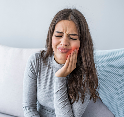 Woman sitting on couch rubbing jaw in pain