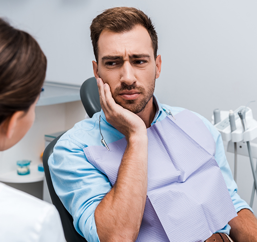 Man with toothache in dental chair looking at dentist