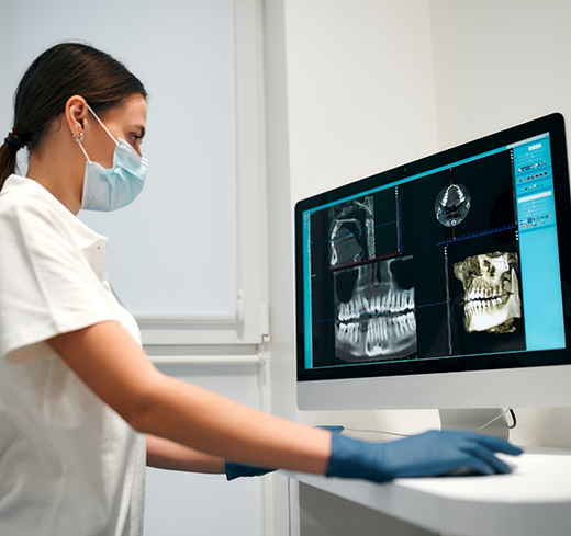 Dental team member with mask looking at X rays on computer monitor
