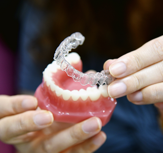 Hands holding clear aligner and model of teeth