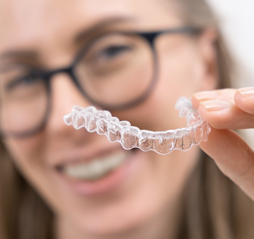 Woman with glasses holding clear aligner
