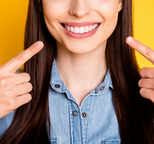 Woman in denim jacket pointing to her smile